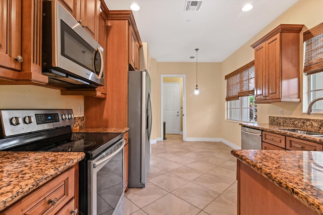 kitchen with appliances with stainless steel finishes, sink, light tile patterned floors, stone countertops, and decorative light fixtures