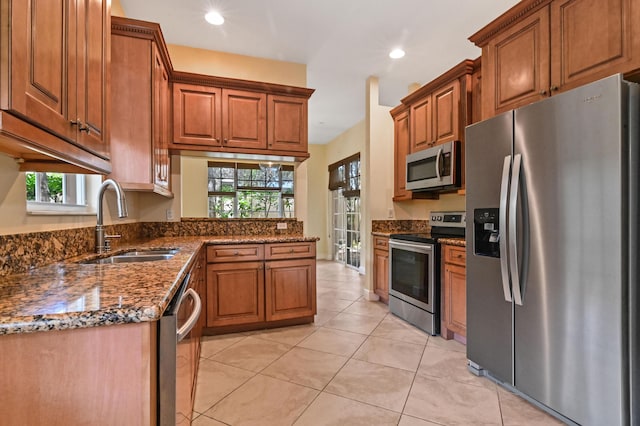 kitchen with dark stone counters, sink, light tile patterned floors, and stainless steel appliances