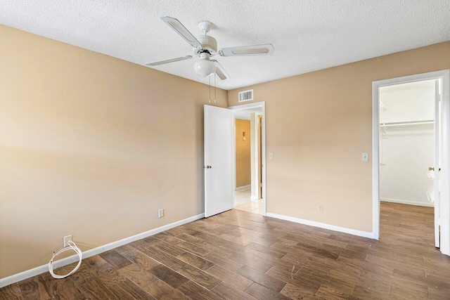 unfurnished bedroom featuring dark hardwood / wood-style flooring, a walk in closet, a textured ceiling, ceiling fan, and a closet