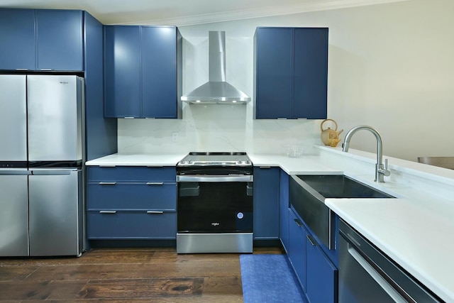 kitchen featuring wall chimney range hood, sink, blue cabinets, dark hardwood / wood-style flooring, and stainless steel appliances