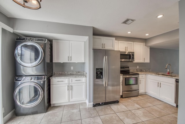 kitchen with white cabinets, light stone countertops, stainless steel appliances, and stacked washer / dryer