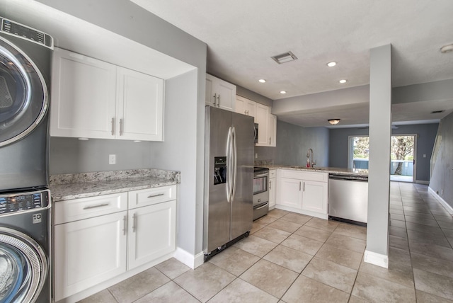 kitchen featuring stainless steel appliances, white cabinets, light stone counters, stacked washer / drying machine, and light tile patterned floors