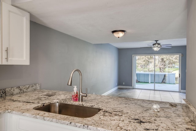 kitchen featuring sink, ceiling fan, light stone countertops, light tile patterned floors, and white cabinetry