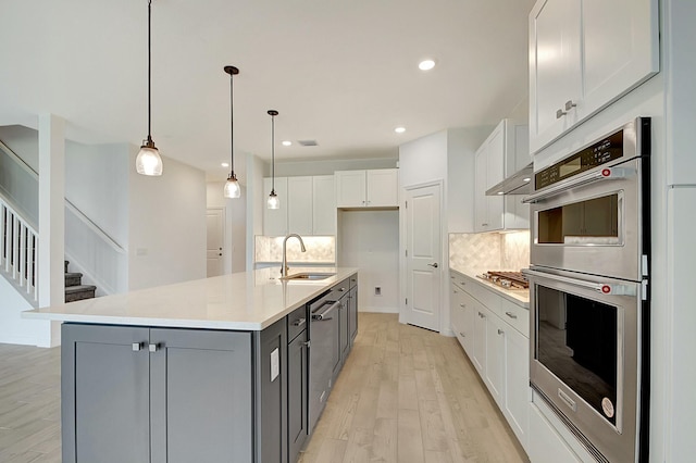 kitchen featuring a center island with sink, sink, hanging light fixtures, appliances with stainless steel finishes, and tasteful backsplash