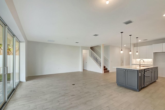 kitchen featuring tasteful backsplash, a kitchen island with sink, sink, white cabinets, and hanging light fixtures