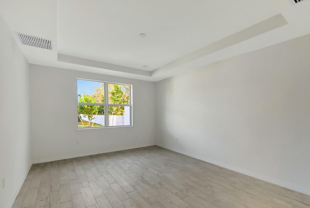 unfurnished room with light wood-type flooring and a tray ceiling