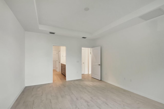 unfurnished bedroom with ensuite bathroom, a raised ceiling, and light hardwood / wood-style floors