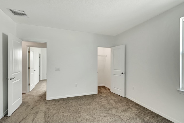 unfurnished bedroom with a walk in closet, a closet, and carpet