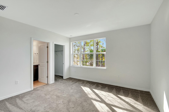 unfurnished bedroom featuring a walk in closet, connected bathroom, light colored carpet, and a closet