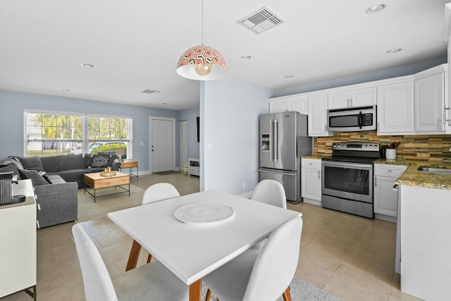 kitchen with white cabinets, hanging light fixtures, decorative backsplash, light tile patterned flooring, and stainless steel appliances