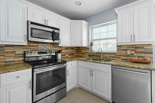 kitchen featuring stainless steel appliances, white cabinetry, dark stone countertops, and sink