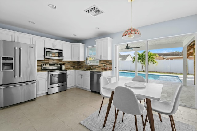 kitchen featuring decorative backsplash, white cabinetry, pendant lighting, and appliances with stainless steel finishes