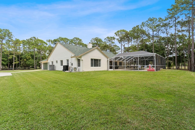 rear view of property with central air condition unit, glass enclosure, a yard, and a garage