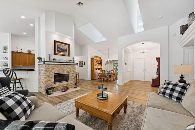 living room featuring a stone fireplace, high vaulted ceiling, a chandelier, and light hardwood / wood-style floors