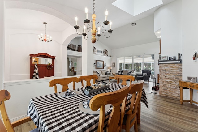 dining area with vaulted ceiling with skylight, wood-type flooring, and an inviting chandelier