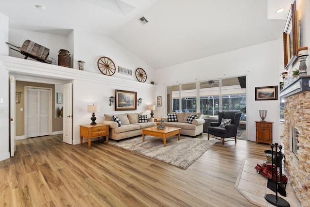 living room with a stone fireplace, light wood-type flooring, and high vaulted ceiling