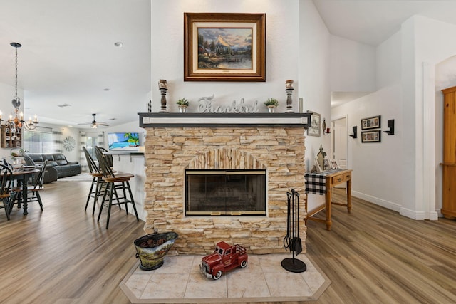 living room with a stone fireplace, ceiling fan with notable chandelier, and hardwood / wood-style flooring