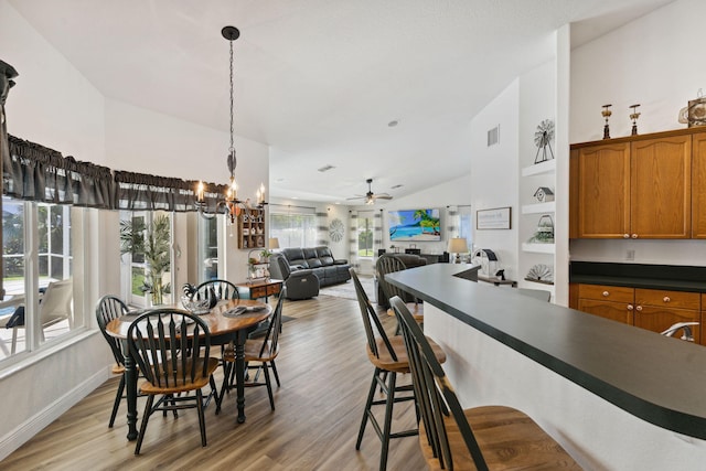 dining room with ceiling fan with notable chandelier, lofted ceiling, and light hardwood / wood-style flooring