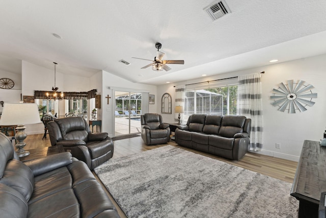 living room featuring ceiling fan with notable chandelier, light hardwood / wood-style floors, vaulted ceiling, and a wealth of natural light