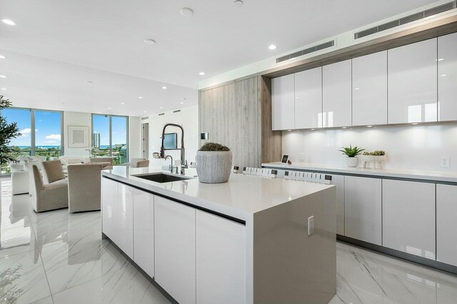 kitchen with expansive windows, a center island with sink, white cabinets, and sink