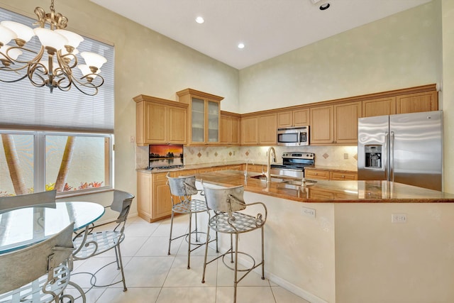 kitchen with sink, a towering ceiling, pendant lighting, a center island with sink, and appliances with stainless steel finishes