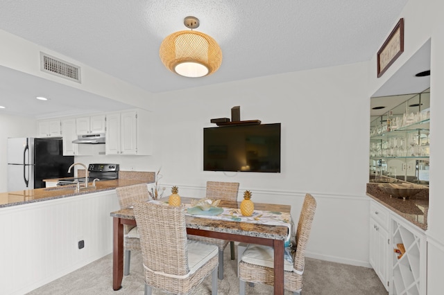 carpeted dining room with sink and a textured ceiling