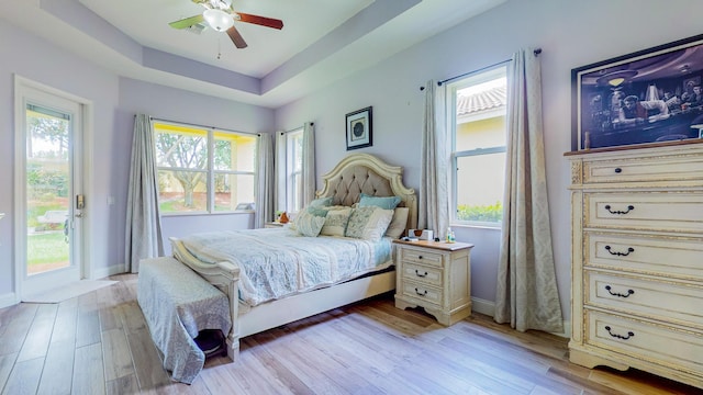 bedroom featuring ceiling fan, a raised ceiling, light wood-type flooring, and access to outside