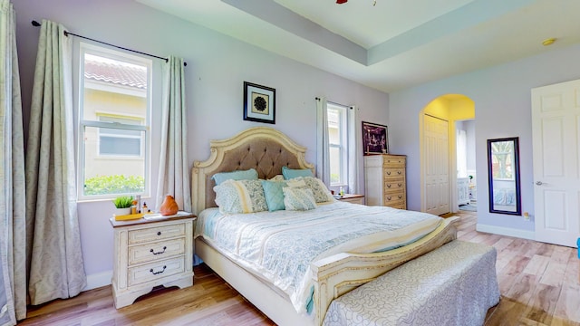 bedroom with light wood-type flooring, a tray ceiling, and a closet