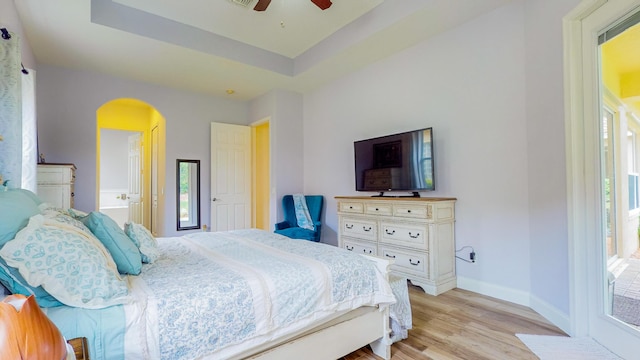 bedroom featuring ceiling fan, a raised ceiling, ensuite bath, and light hardwood / wood-style flooring