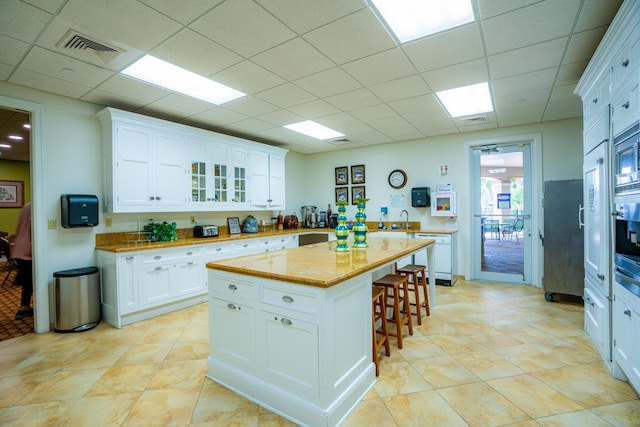 kitchen featuring white cabinetry, a center island, dishwasher, light stone countertops, and a kitchen breakfast bar