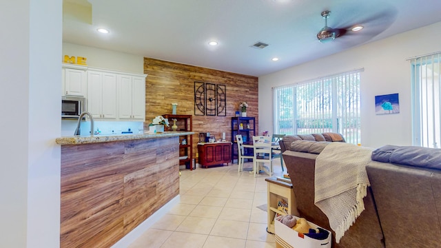 kitchen with light stone countertops, ceiling fan, light tile patterned flooring, wood walls, and white cabinets