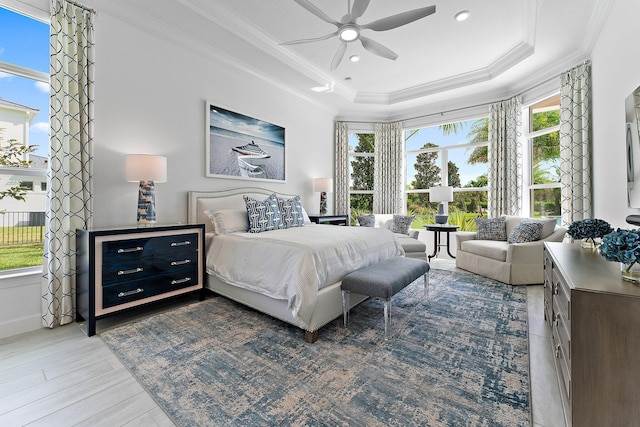 bedroom with light wood-type flooring, a tray ceiling, ceiling fan, and crown molding