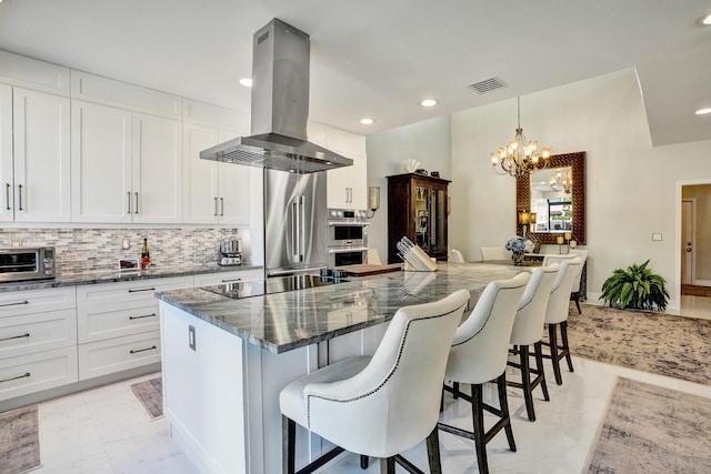 kitchen featuring a kitchen breakfast bar, island range hood, white cabinetry, and appliances with stainless steel finishes