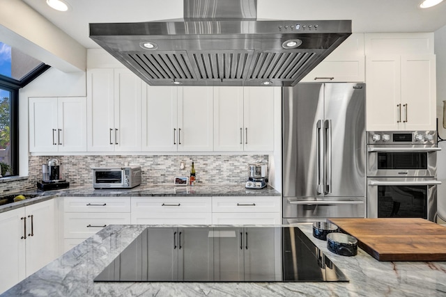 kitchen with white cabinets, appliances with stainless steel finishes, tasteful backsplash, and wall chimney exhaust hood