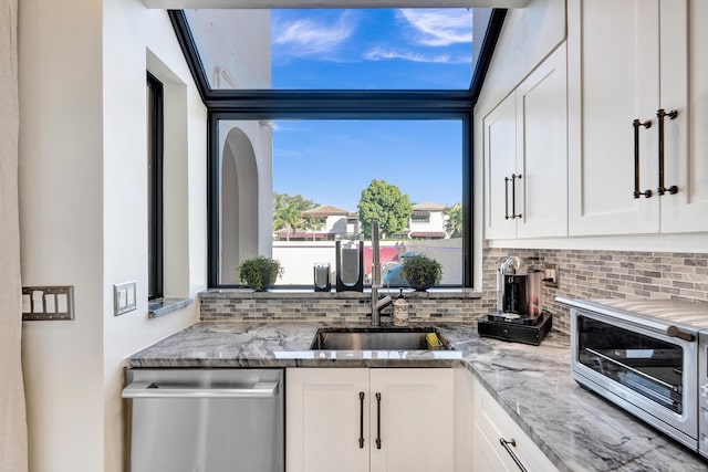 kitchen with backsplash, white cabinetry, dishwasher, and light stone countertops