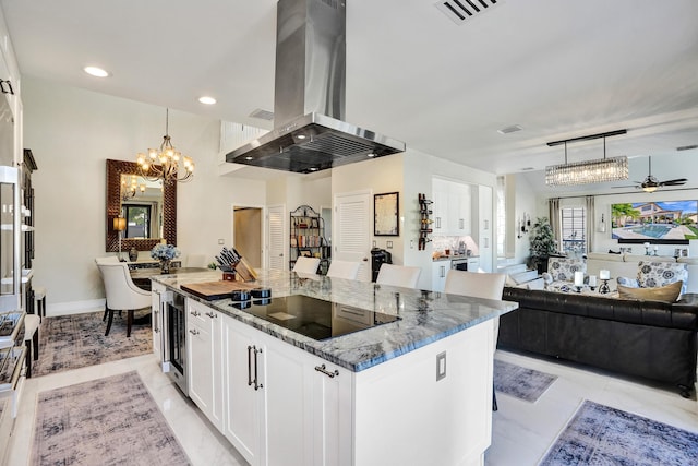 kitchen with black electric stovetop, decorative light fixtures, white cabinetry, and wall chimney range hood