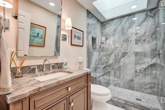 bathroom featuring a skylight, vanity, a shower with shower door, and toilet