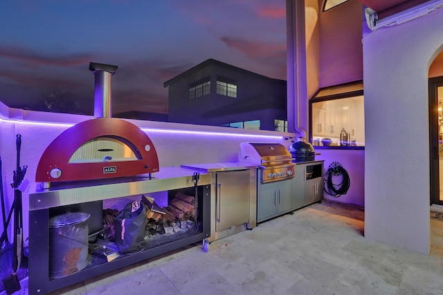 patio terrace at dusk featuring area for grilling and exterior kitchen