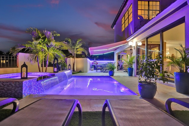 pool at dusk featuring pool water feature, a patio area, and an in ground hot tub