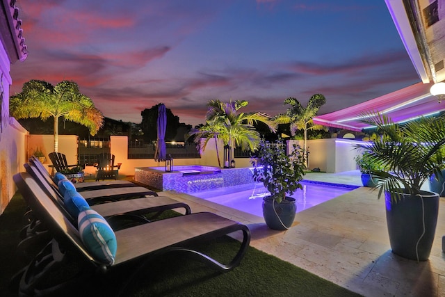 pool at dusk featuring an in ground hot tub and a patio area