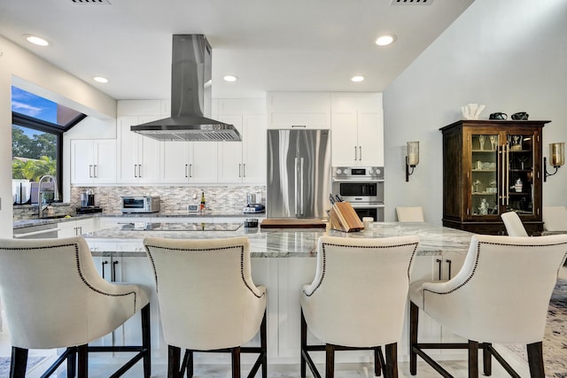 kitchen with a center island, appliances with stainless steel finishes, tasteful backsplash, white cabinetry, and island exhaust hood