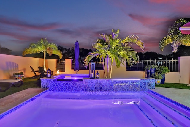 pool at dusk featuring an in ground hot tub and a patio