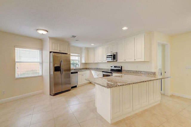 kitchen featuring light stone countertops, sink, stainless steel appliances, kitchen peninsula, and white cabinets