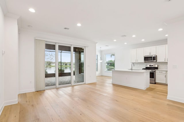 kitchen with crown molding, white cabinets, a kitchen island with sink, and appliances with stainless steel finishes