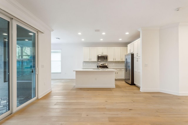 kitchen with tasteful backsplash, a center island with sink, light wood-type flooring, appliances with stainless steel finishes, and white cabinets