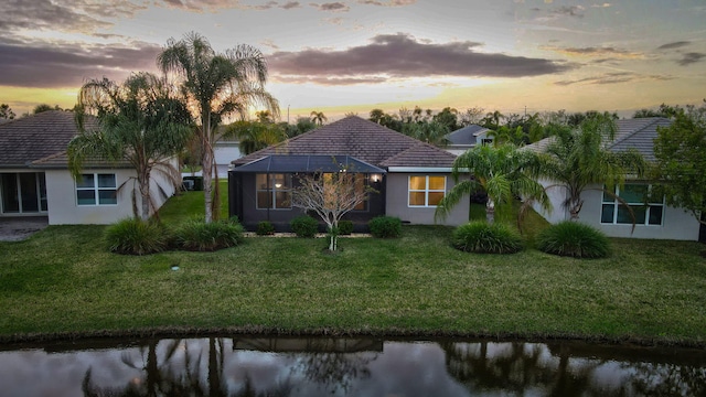 view of front of house featuring a lawn, a water view, and glass enclosure