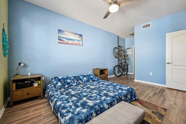 bedroom with ceiling fan, wood-type flooring, and a textured ceiling