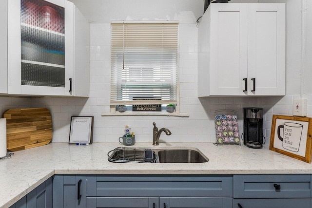 kitchen with light stone counters, backsplash, blue cabinetry, white cabinets, and sink