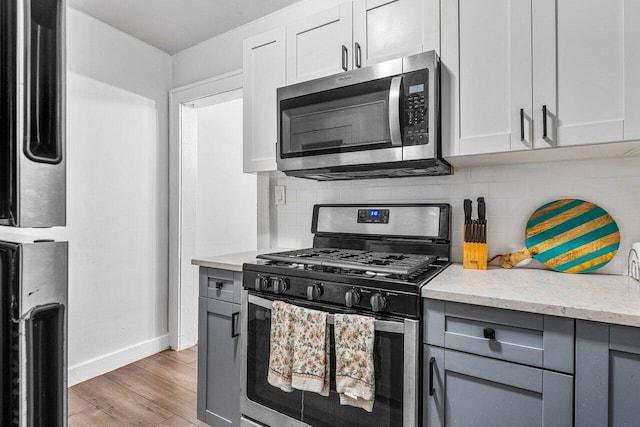 kitchen featuring light stone counters, stainless steel appliances, tasteful backsplash, light wood-type flooring, and white cabinetry