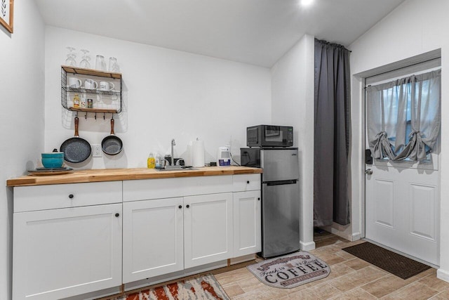 kitchen with white cabinets, stainless steel refrigerator, sink, and butcher block counters